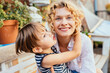 © Iryna - Blond curly excited happy woman and her son hugging together at garden or backyard. Cute little boy kissing her mother on terrace at summer day.