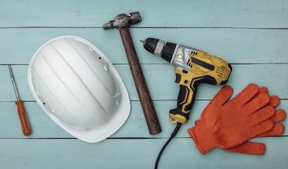 Wall Mural - Old drill screwdriver and protective helmet, gloves and work tool on blue wooden background. Top view