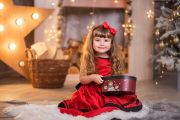 Wall Mural - Little beautiful girl in a red dress near the Christmas tree. Girl with a doll are playing Christmas. The child smiles. Beautiful girl with long curly hair. child in santa claus clothes