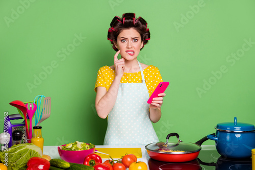 Portrait of her she nice attractive confused nervous funky housewife cooking fresh meal dish find recipe biting lip blogging isolated over green pastel color background