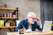 © Face Stock - Focused older man in smart casual wear is using laptop computer for watching online classes and webinars, he is takes a notes at notebook, while sitting at contemporary home office