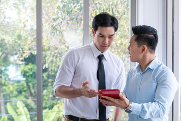 Two businessmen working at the office. Serious coworkers holding using digital tablet discussing corporate strategy with device in modern office. Two business people discussing something seriously.