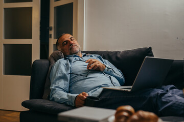 middle aged man sitting sofa and resting using laptop computer at home