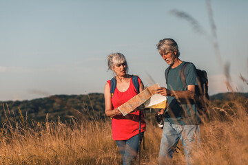 Wall Mural - Active senior couple hiking in nature with backpacks, enjoying their adventure at sunset.	