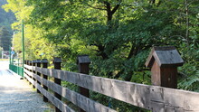 Rustic Wooden Fence Stretching Along A Bridge Over A River In A Green Sunny Park, Extending In A Linear Perspective
