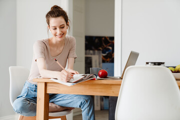 Photo of smiling student girl in earphones doing homework with laptop