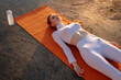 Image of redhead nice sportswoman using earphones while lying on mat
