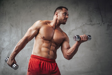 Wall Mural - Seductive and muscualr guy with naked torso lifting iron dumbells in special grung background of studio.