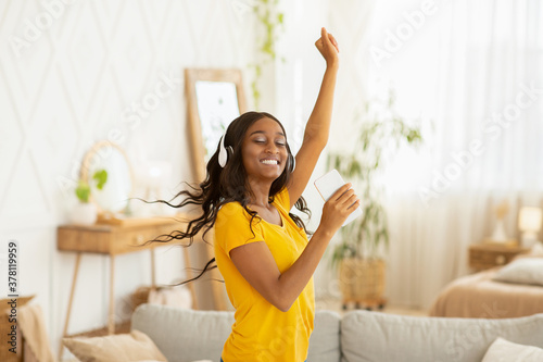 Happy young black woman with headphones and mobile device dancing to her favorite music at home