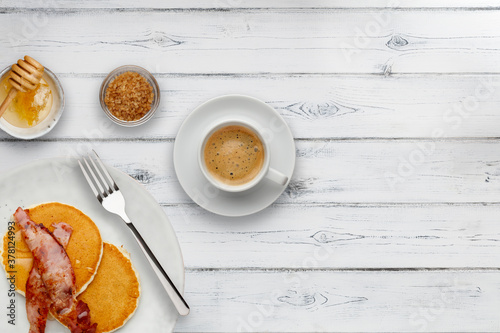 A plate of bacon and pancakes, drizzled with honey, a cup of coffee nad bowl of Tableau sur Toile