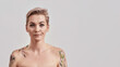 Well... Portrait of a young attractive half naked tattooed woman with short hair looking with smirk at camera being disappointed or unimpressed isolated over light background