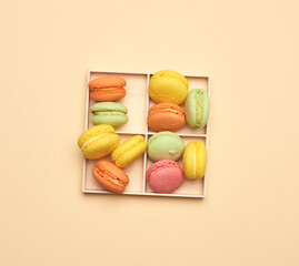 Wall Mural - wooden box and baked multi-colored macarons cookies on a beige background