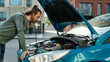 © Svitlana - Young man looking focused, examining his broken car with open hood while standing on the city street