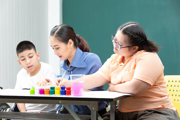 asian disabled kids or autism child learning and painting at paper with teacher helping in classroom