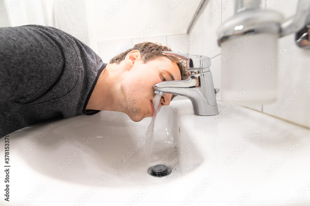 young man drink tap water by mouth out of sink in bathroom with lips and tongue in flowing water being totally thirsty and can't get enough liquid may be a symptom for sickness or diabetes