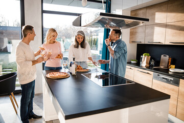 Wall Mural - Happy men and women eating pizza in the kitchen