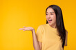 © Nutlegal - Happy beautiful young asian woman with yellow background holding copy space imaginary on beauty palm for insert advertisement, happiness and smiley face. Attractive beautiful girl portrait