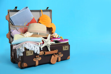 Sticker - Packed vintage suitcase with different beach objects on light blue background, space for text. Summer vacation