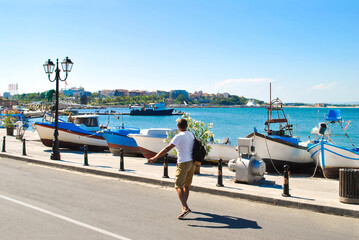 Man with backpack walking along seafront past fishing boats at sunny light day