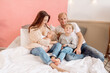 © Maria - Beautiful young family: mom, dad, daughter and son are sitting on the bed at home in a bright bedroom and hugging