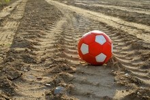 Used Red And White Soccer Ball On Dirty Earth