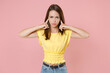 © ViDi Studio - Displeased concerned young brunette woman 20s wearing yellow casual t-shirt posing standing covering ears with fingers looking camera isolated on pastel pink color wall background studio portrait.