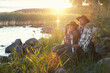 © Gargonia - Couple man and woman in felt hats wrapped in wool blanket sitting near lake on sunset. Weekend picnic on nature, local travel, staycation, folk lifestyle.