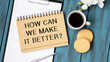 Text sign showing How Can We Make It Better question. Conceptual photo asking how increase quality of product Man holding marker notebook clothespin reminder wooden table cup coffee.