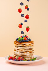 Canvas Print - Pancakes stack with levitation of strawberries and blueberries.