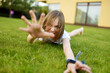 Funny young girl having fun on a grass on the backyard on sunny summer evening.
