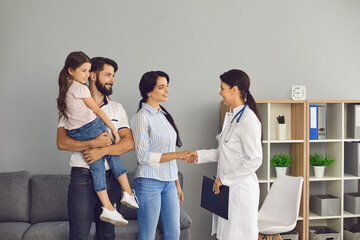 Wall Mural - Happy family saying goodbye to woman doctor and shaking hands after successful visit in medical clinic