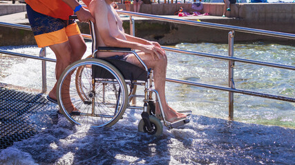 Wall Mural - Accessible beach with ramp for disabled people. Man on wheelchair going swimming.