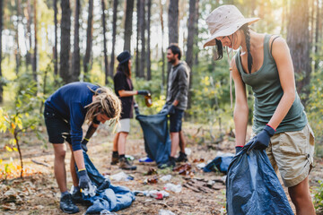 Group of volunteer people picking up plastic in forest, caring for nature, cleaning in park, outdoor trash and rubbish.