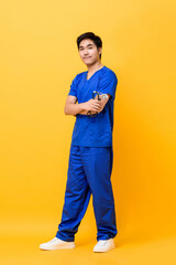 Full length portrait of smiling young Asian man nurse with arms crossed holding stethoscope in isolated studio yellow background