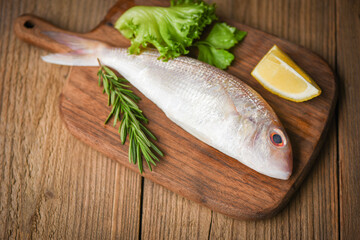 Wall Mural - Fresh raw fish with ingredients  lemon rosemary and lettuce for making cooked food on wooden cutting board - sea bream seafood fish frozen