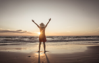 Woman in red with arms outstretched by the sea at sunrise enjoying freedom and life