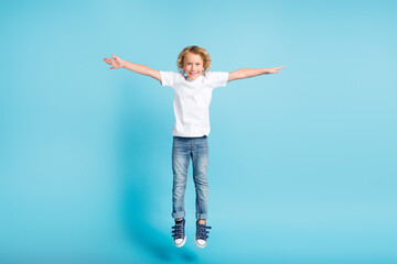 Photo of little boy jump raise hands wings wear white shirt jeans sneakers isolated blue color background