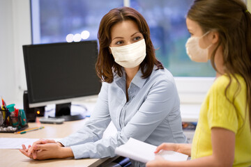 Poster - education, school and pandemic concept - teacher and little student girl wearing face protective medical masks for protection from virus disease in classroom