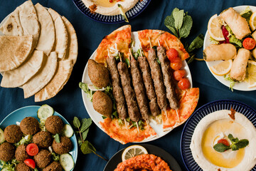 Wall Mural - Traditional Arab cuisine including kebab meat, kibbeh, mutabal, falafel, muhammara, pita bread and hummus