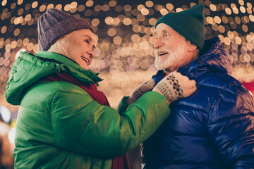 Photo of two people retired pensioner prepare for x-mas christmas jolly holly tradition town center walk woman fix adjust button husbands outerwear under outside advent lights