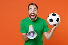 Surprised Young Man Football Fan In Green T-shirt Cheer Up Support Favorite Team With Soccer Ball Screaming In Megaphone Isolated On Orange Background Studio. People Sport Leisure Lifestyle Concept.