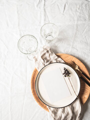 Tableware and decorations for serving table. Ceramic and wooden plates, wine glasses and cutlery with linen napkin on white tablecloth background.