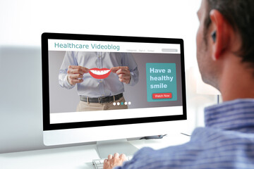 Back view of man using computer with health videoblog on the screen