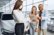 © fotofabrika - Car saleswoman wearing medical mask shows buyers couple something on digital tablet