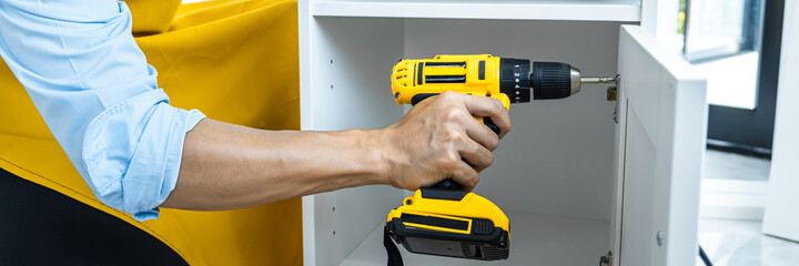 Man doing renovation work at home drilling wood with drill tack on locker