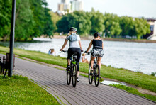 Cyclists Ride On The Bike Path In The City Park
