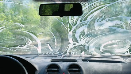 Wall Mural - A man cleans his car with a microfiber cloth. Car wash with soap on the street. Car in foam. Inside view