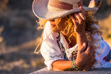 Portait Of Beautiful Young Trendy Woman With Cowboy Hat And Accessories Like Bracelets Lay Down On A Wall Bench Enjoying The Sunset Light - People In Outdoor Leisure Activity And Vacation Time