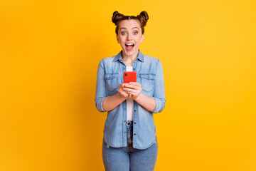 Poster - Photo of funny teen lady two buns look interested telephone read positive nice good comments blog open mouth overjoyed shocked wear casual denim shirt isolated yellow color background