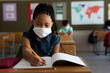 © Wavebreak Media - Mixed Race Girl wearing face mask writing while sitting on her desk at school